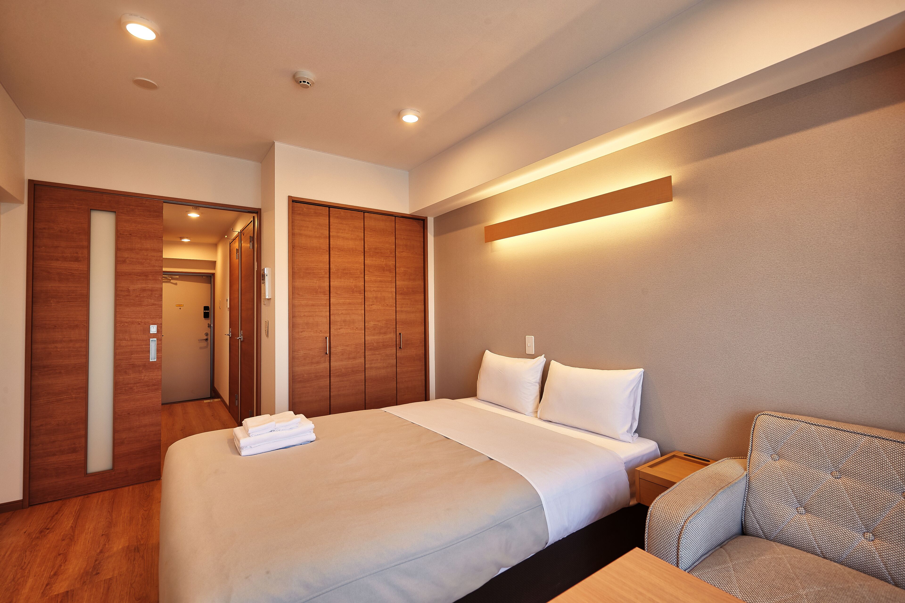 Una habitación de hotel con una cama grande, un armario de madera, una mesita de noche y un sofá.