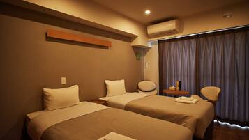 A hotel room with two beds, a round table with a chair, an air conditioning unit, and a window with curtains.