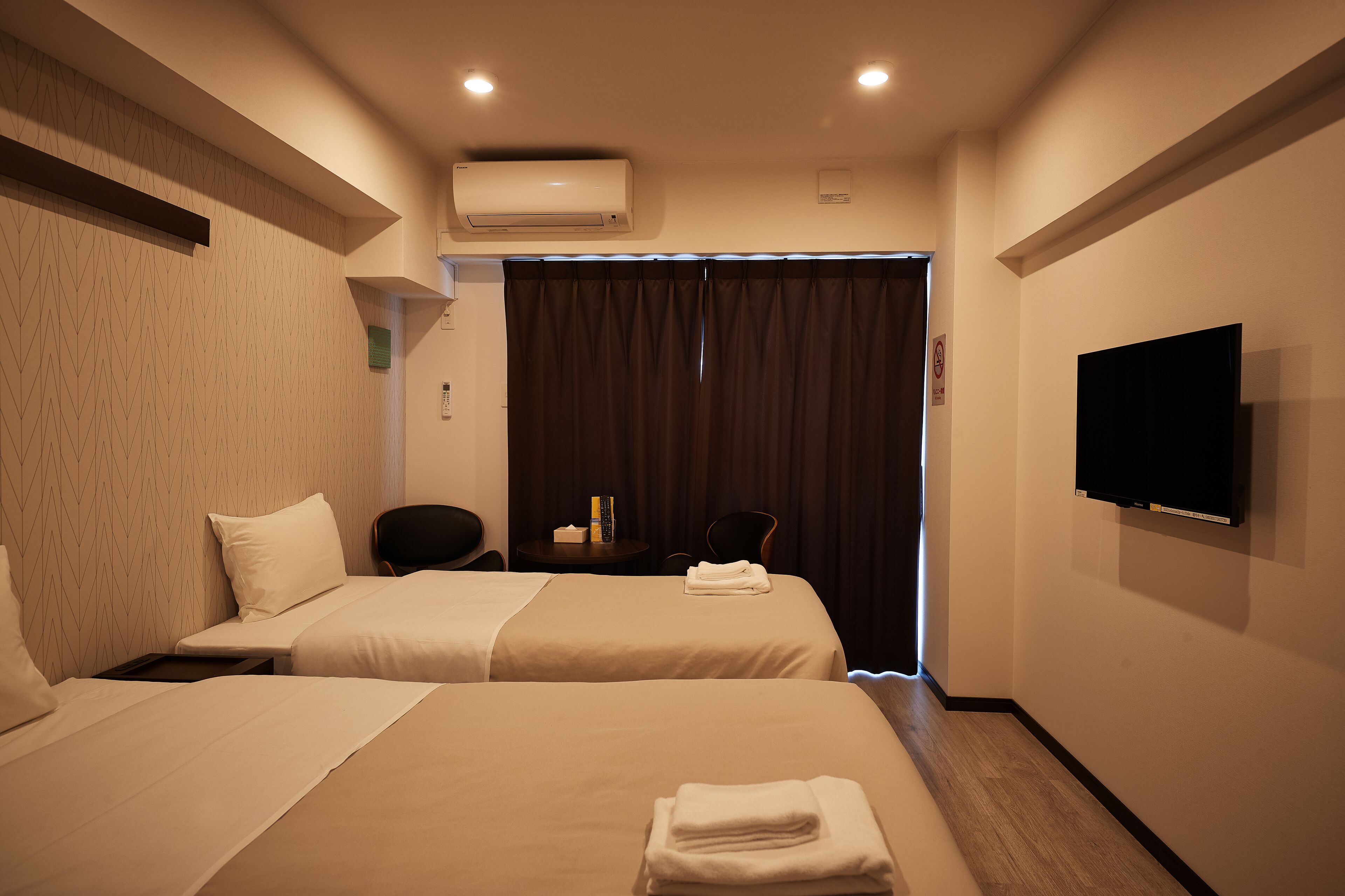 Une chambre d’hôtel avec deux lits, une télévision, la climatisation et un bureau avec une chaise.