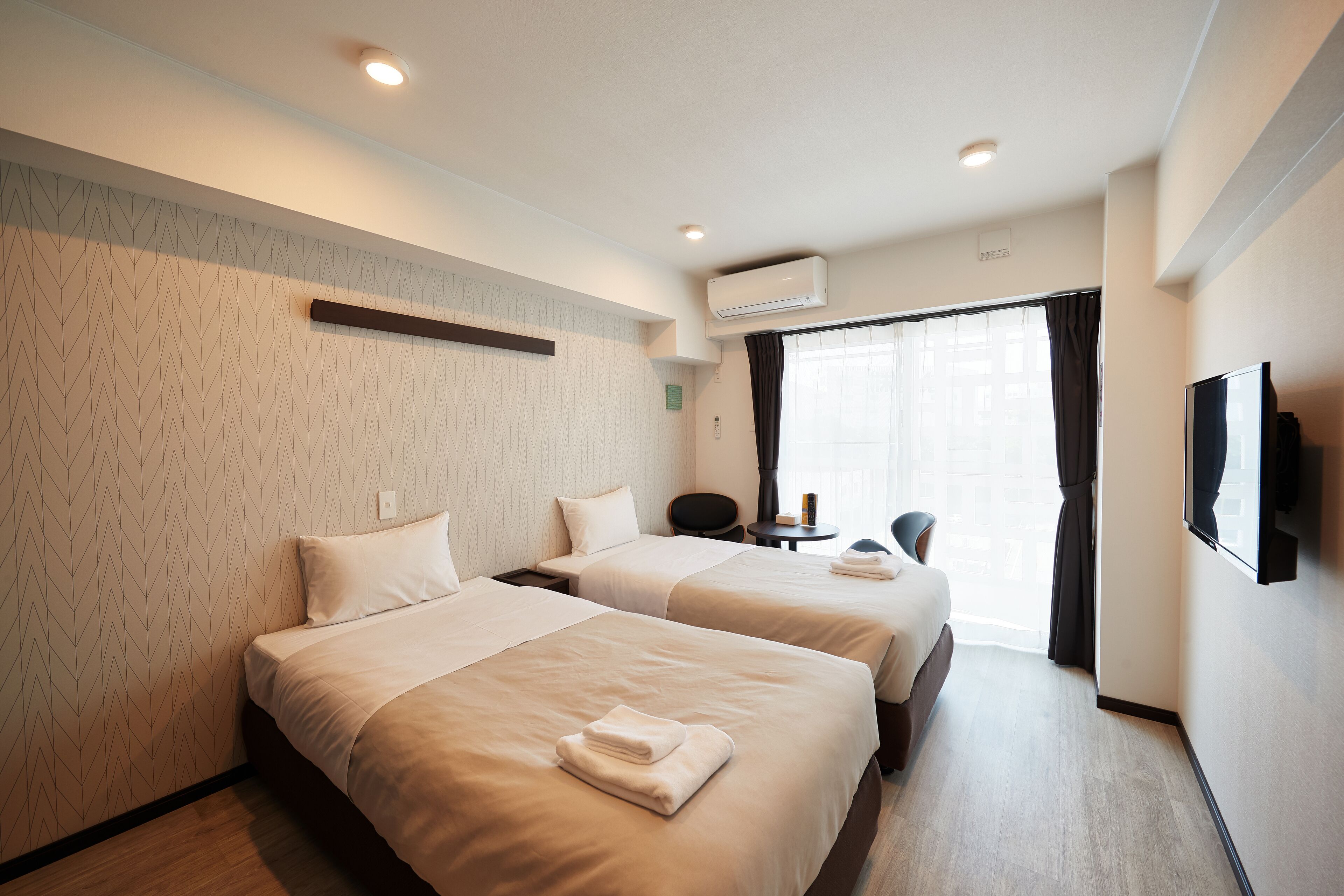A hotel room with two beds, a flat-screen TV, a desk, and a window with curtains.