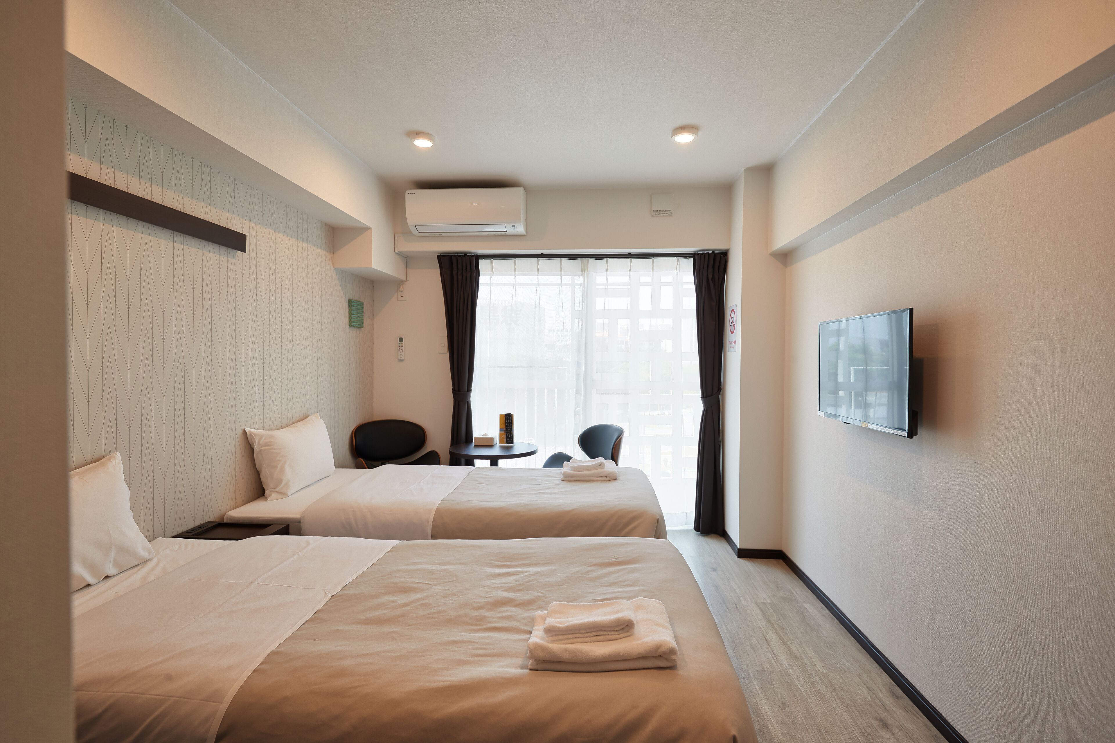 A hotel room with two beds, a desk, a chair, a TV, and a window with curtains.