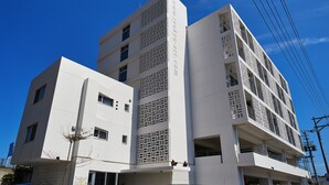 A modern multi-story building with a prominent vertical design element and a website address on the facade. - Arce Ryukyu Harbor Stay (Urasoe)