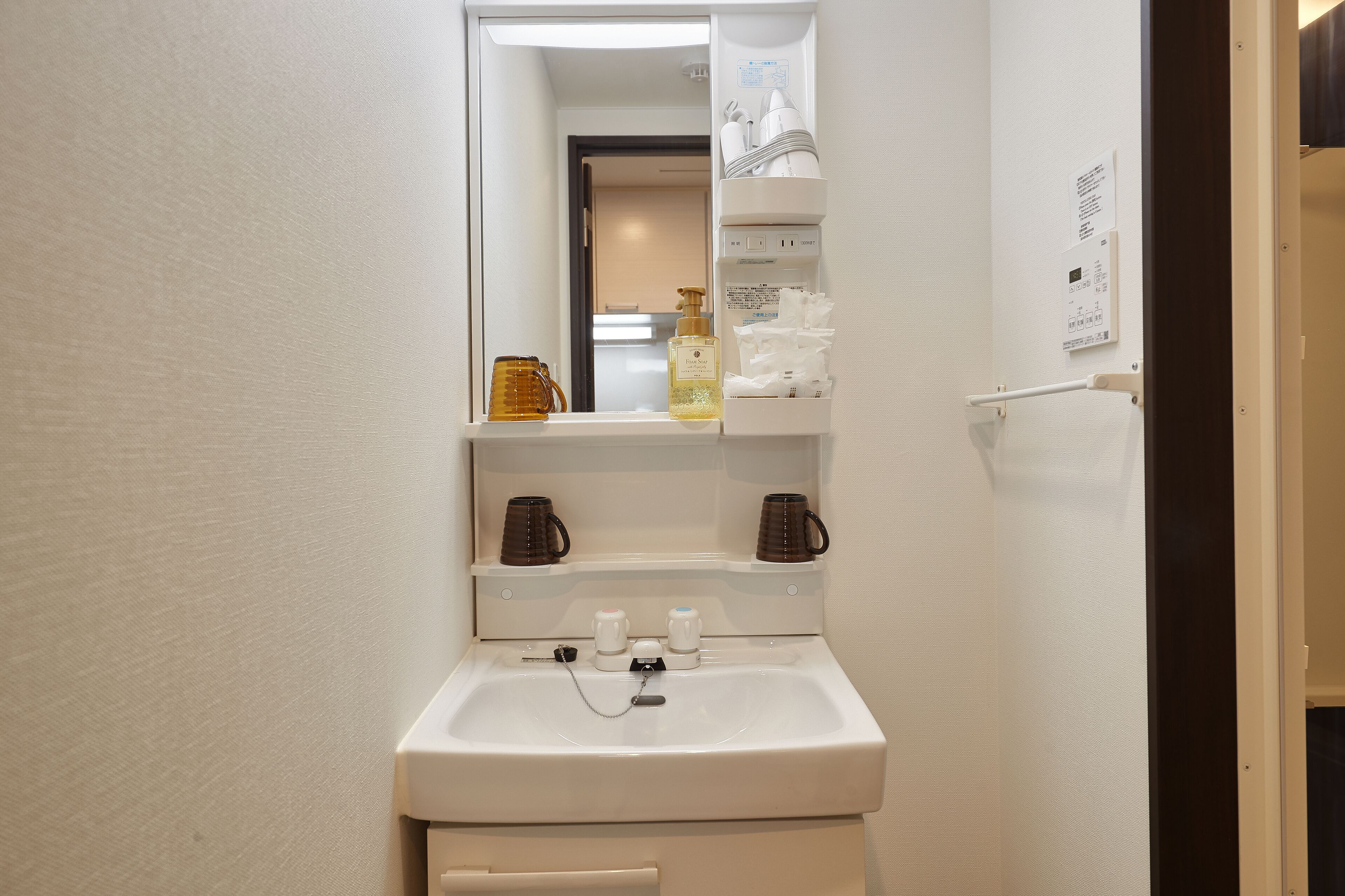Un baño con un lavabo blanco, un espejo y estantes sobre el lavabo con artículos de tocador y una botella de jabón para manos.