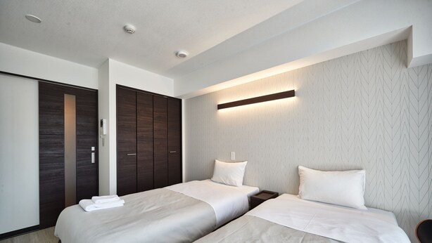 A hotel room with two beds, a wardrobe, and a wall-mounted light fixture. - Arce Ryukyu Harbor Stay (Urasoe)