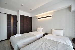 A hotel room with two beds, a wardrobe, and a wall-mounted light fixture. - Arce Ryukyu Harbor Stay (Urasoe)