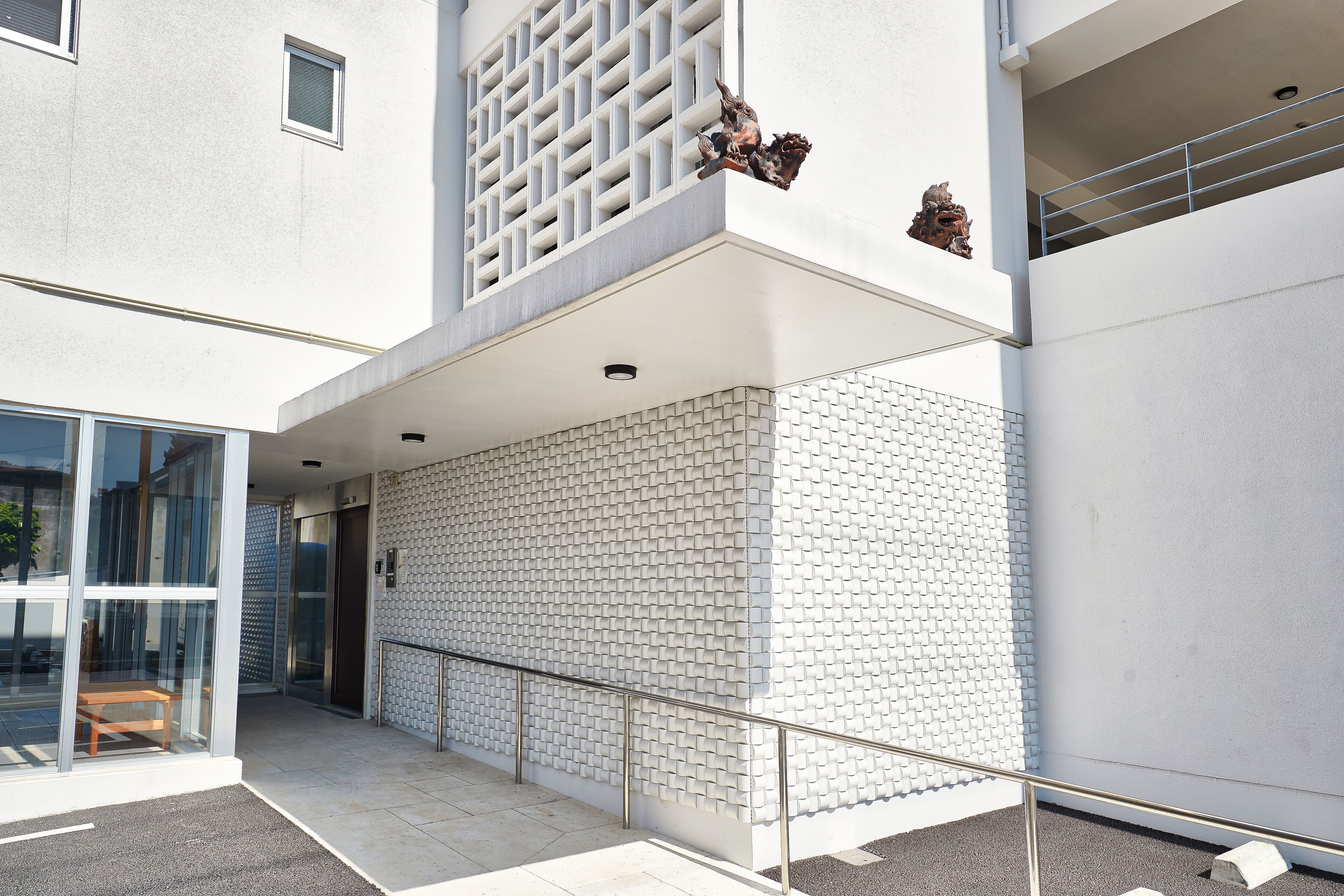 A modern building with a glass entrance, a white brick wall, and a metal railing.