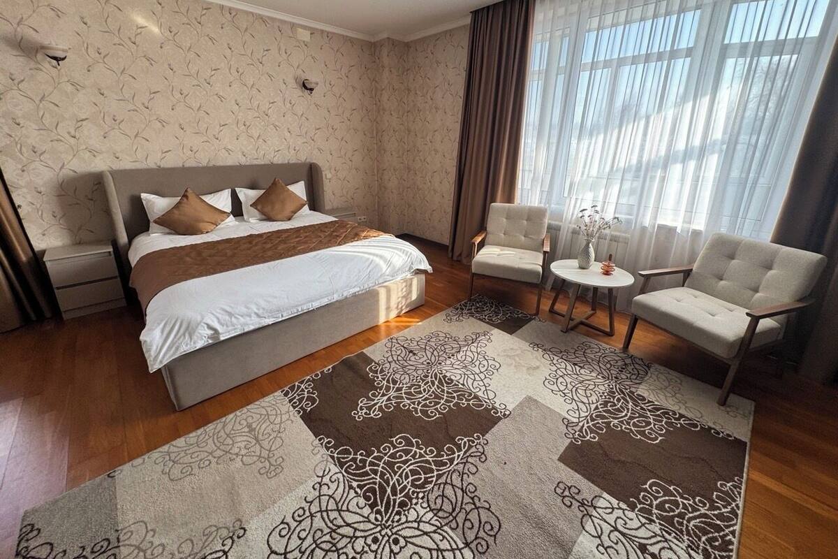 A bedroom with a bed, two armchairs, a small table, and a patterned rug.