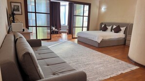 A modern hotel room with a sofa, a bed, a large window, and a view of the outdoors. - Apart Hotel Keremet (Almaty)