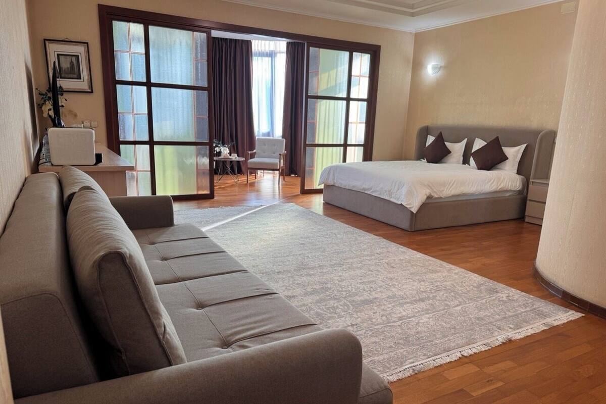 A modern hotel room with a sofa, a bed, a large window, and a view of the outdoors.