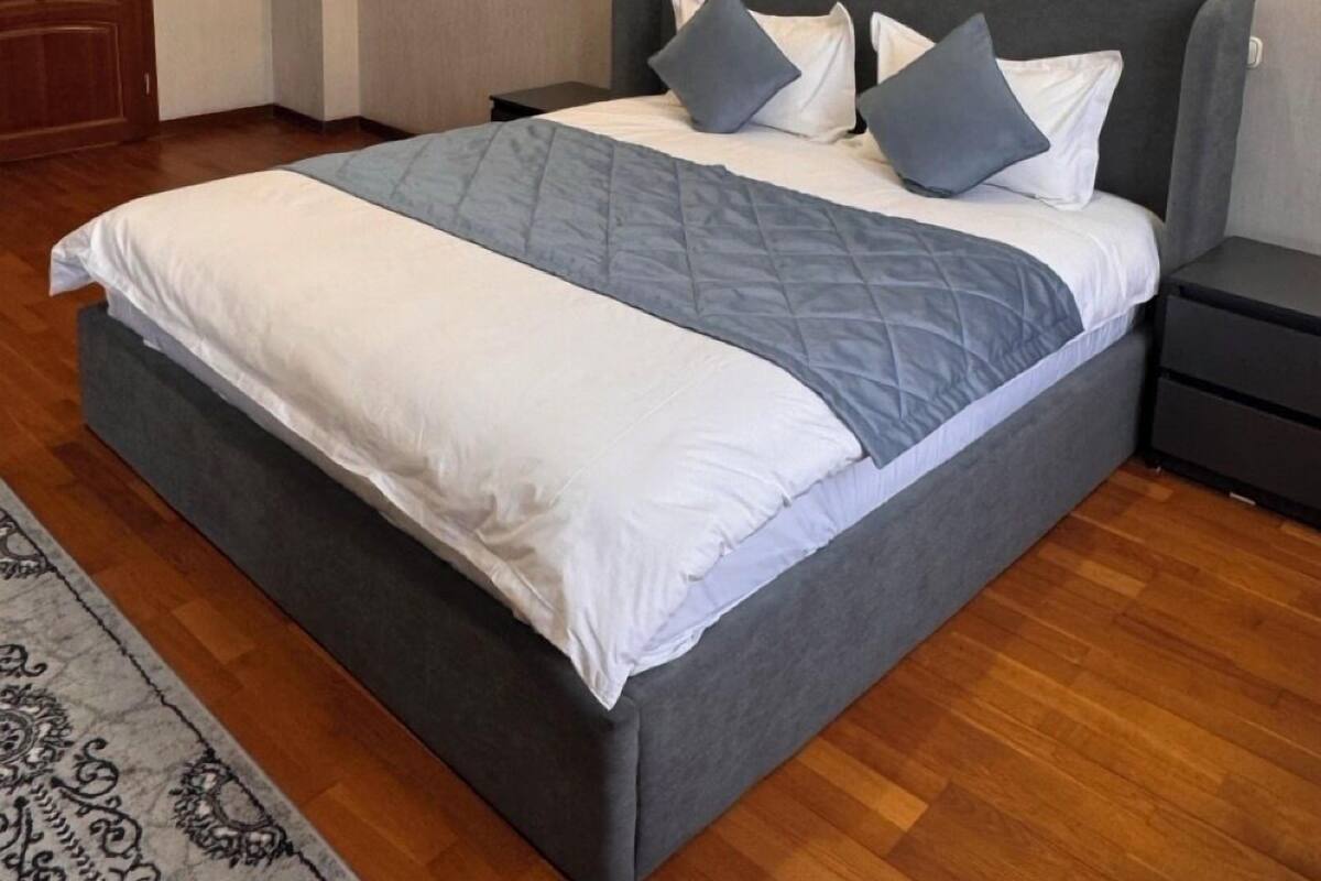 A modern bedroom with a large bed, a nightstand, a wall-mounted light, and a door.