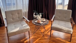 A room with two armchairs and a small round table with a white vase and a plate of food. - Apart Hotel Keremet (Almaty)