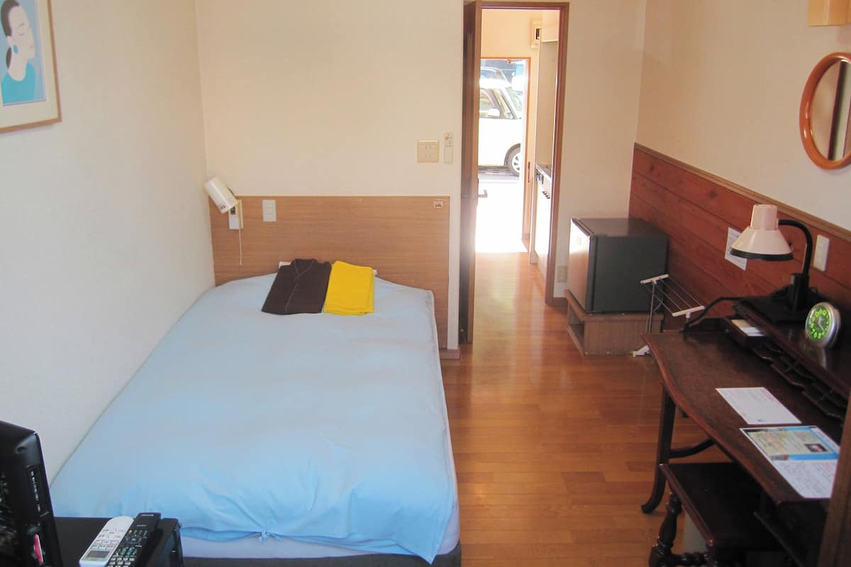 A hotel room with a bed, a desk with a lamp, a TV, and a clock.