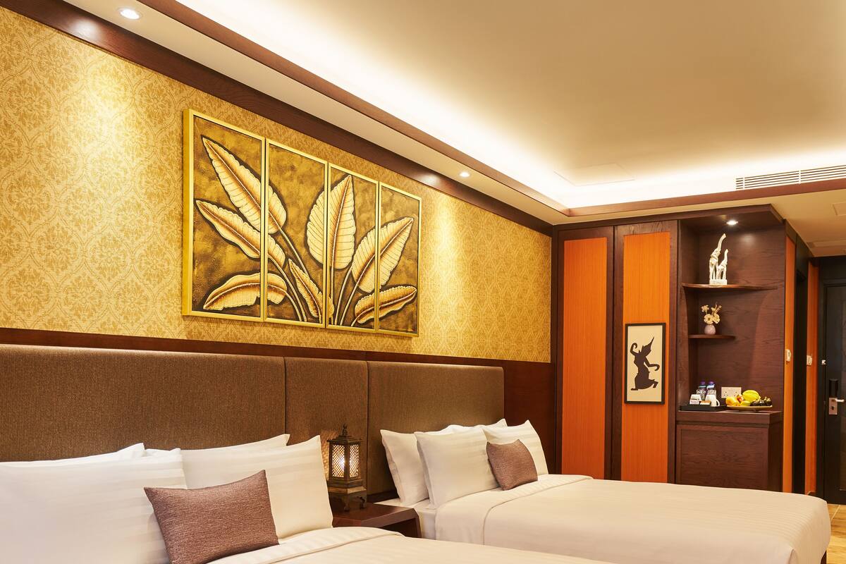A hotel room with two beds, a large decorative wall piece, a nightstand with a lamp, and a wooden cabinet with shelves.
