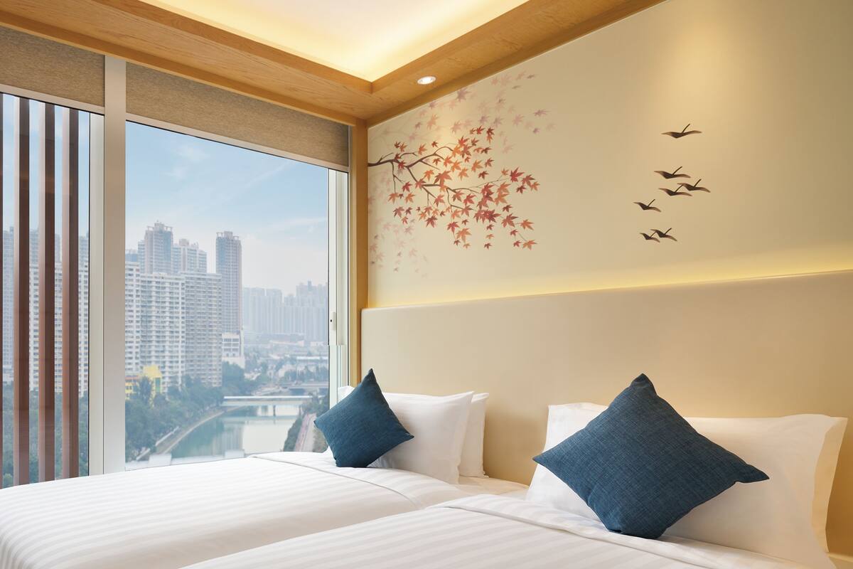 A hotel room with a large bed, two pillows, a city view, and a wall mural.