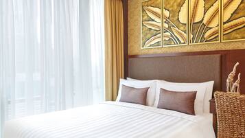 A hotel room with a large bed, a headboard with artwork, a wicker chair, and a view through sheer curtains.