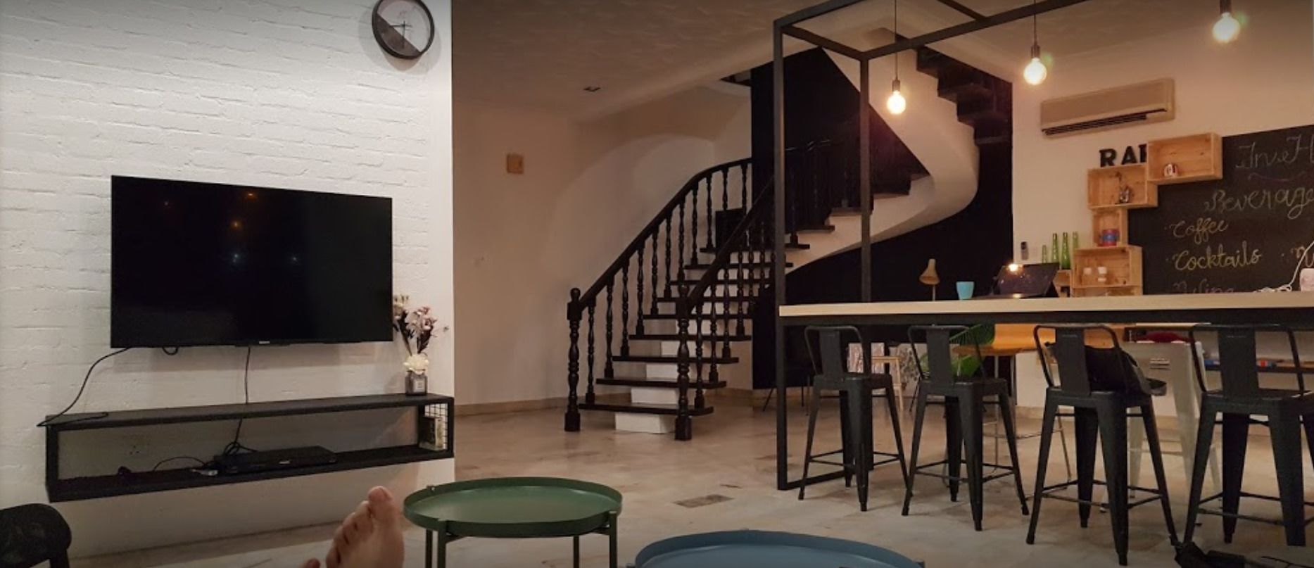 A modern living room with a flat-screen TV, a staircase, and a bar area with stools.