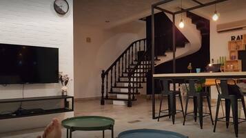 A modern living room with a flat-screen TV, a staircase, and a bar area with stools.