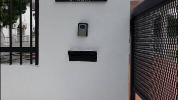 A white building with a black gate, a mailbox, and a sign reading "26 IN HOMS".