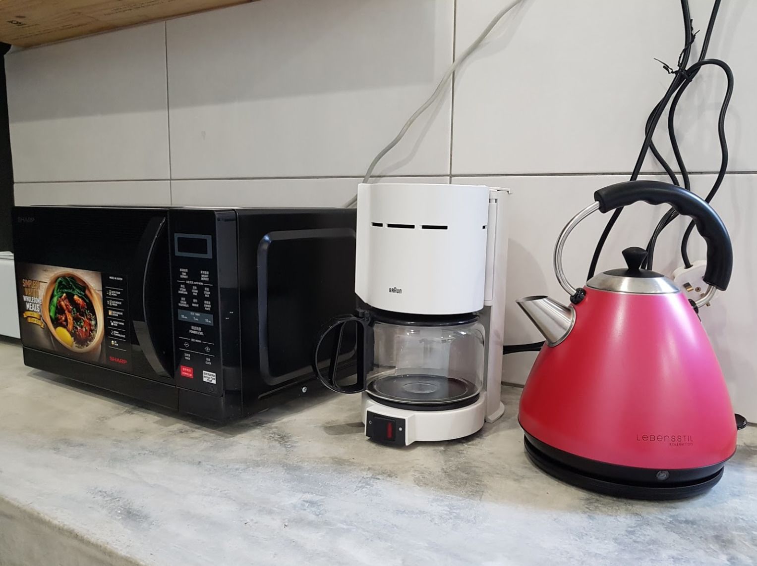 Une cuisine avec un micro-ondes noir, une machine à café blanche et une bouilloire rouge posées sur le plan de travail.
