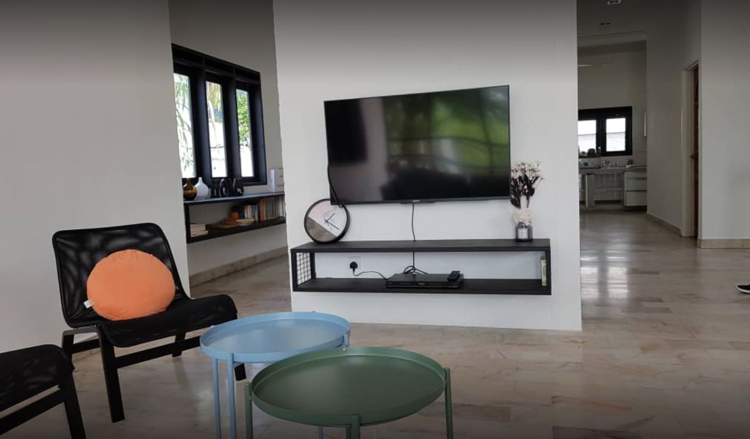 Una sala de estar moderna con una televisión de pantalla plana montada en la pared, una estantería, un reloj y una pequeña mesa.