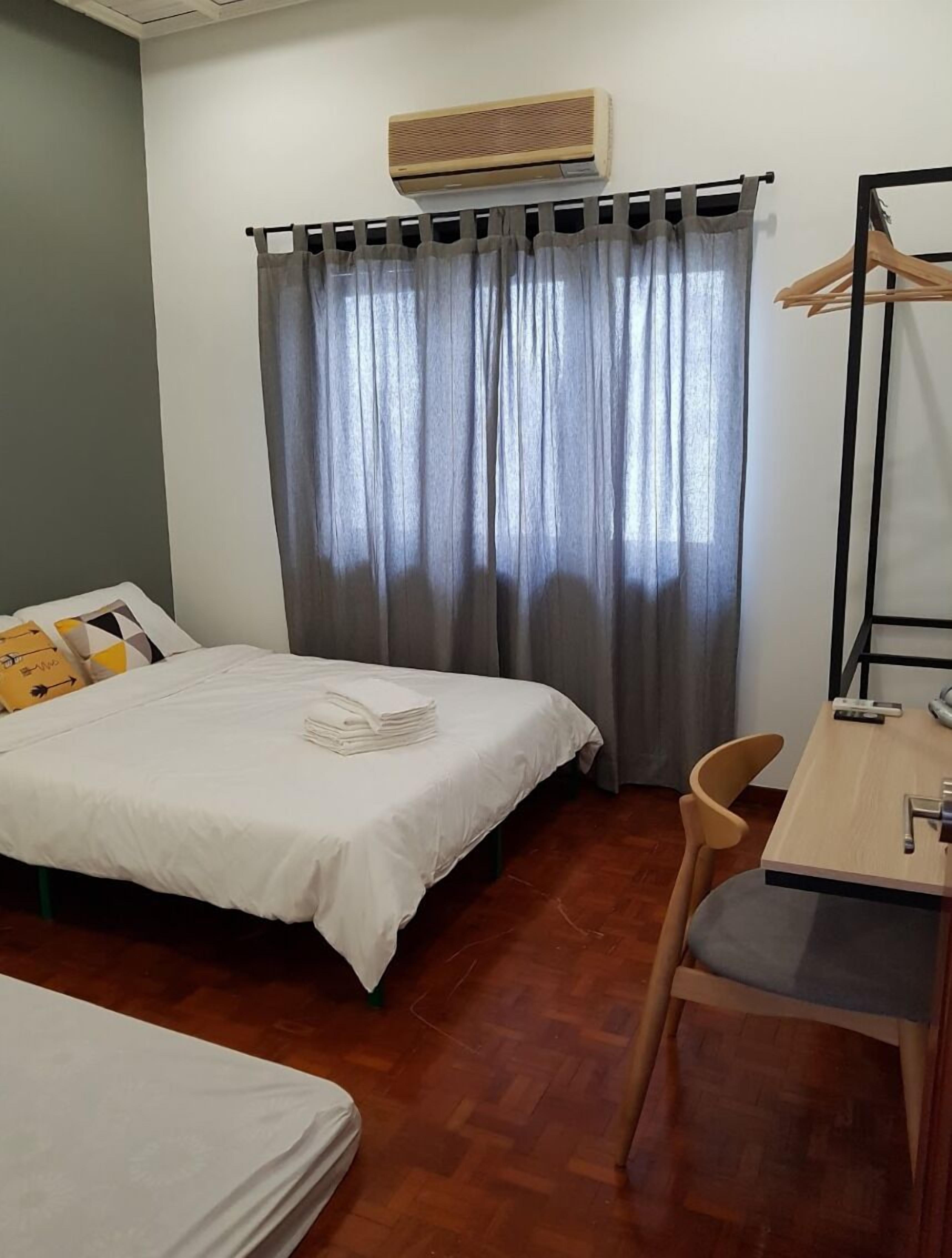 A compact hotel room with a bed, a desk, and a chair. There is an air conditioning unit mounted on the wall above the bed.