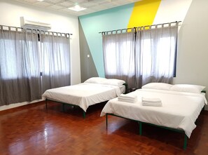 A hotel room with two single beds, a wooden floor, and a ceiling fan.