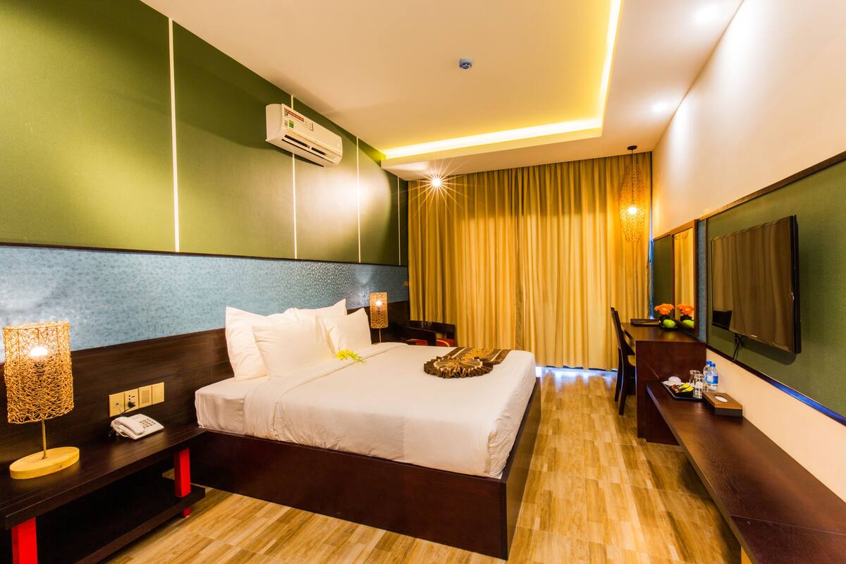 Une chambre d’hôtel avec un grand lit, une table de chevet, une lampe, un appareil de climatisation et un miroir au mur.