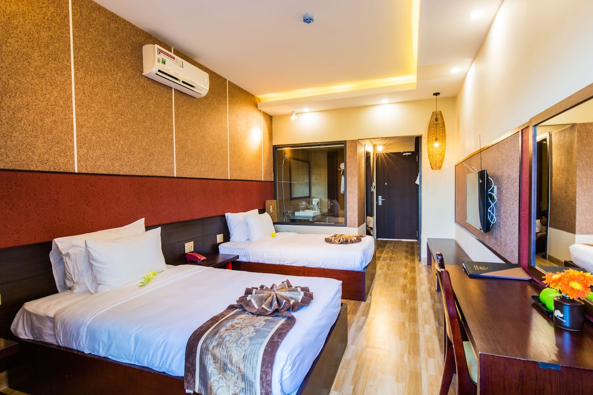 Une chambre d’hôtel avec deux lits, un bureau, un miroir et une grande fenêtre.