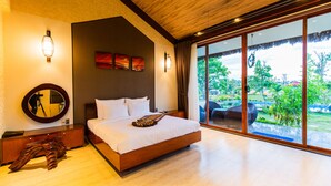 Quarto com uma cama grande, cabeceira de madeira, um espelho, cómoda de madeira e vista para o exterior através de grandes janelas.