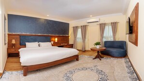 A hotel room with a large bed, a wooden nightstand, a round table with a plant, a blue sofa, and a TV mounted on the wall. - Hotel Boutique Lacoul Inn (Siddharthanagar)