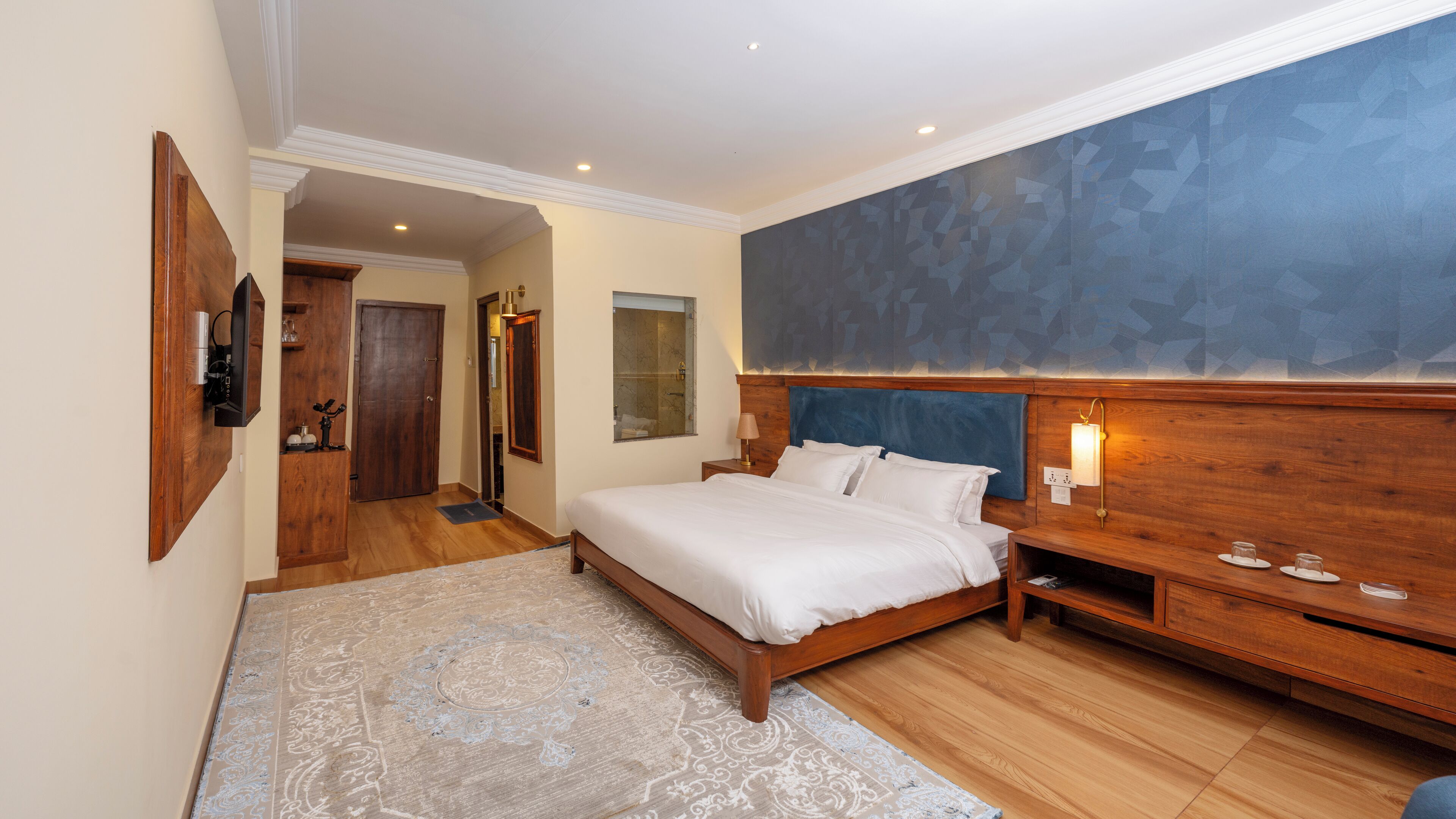 Een slaapkamer met een groot bed, houten hoofdbord, nachtkastjes, een vloerkleed en een groot raam met uitzicht.