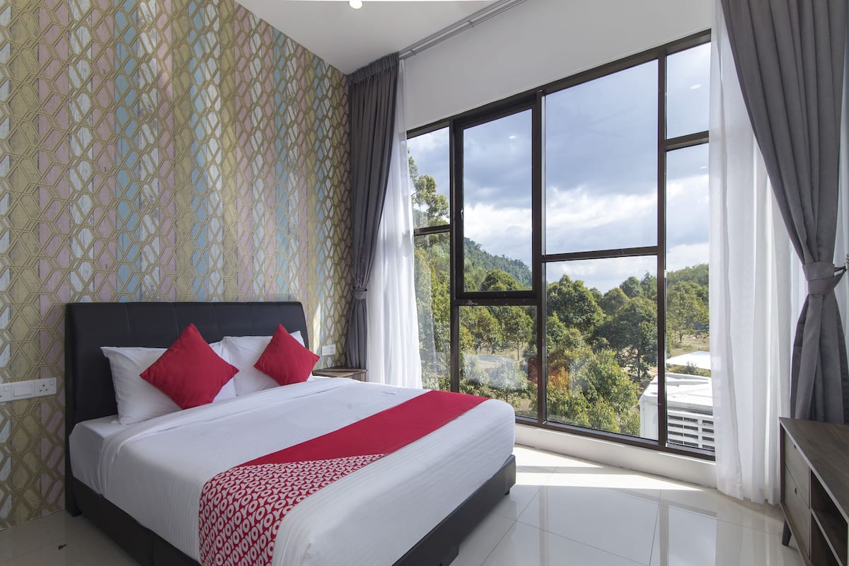 A bedroom with a large bed, a view of greenery outside, and a patterned wall.