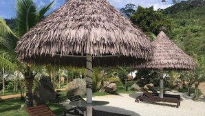 Een strandsetting met rieten parasols, lounge fauteuils en een grindpad.