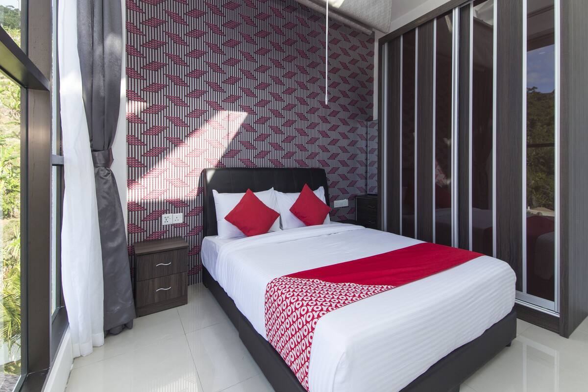 A modern bedroom with a large bed, a wardrobe, and a view of greenery.