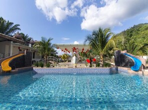 A swimming pool with slides, palm trees, and a building with a thatched roof. - Rock Mountain (Raub)