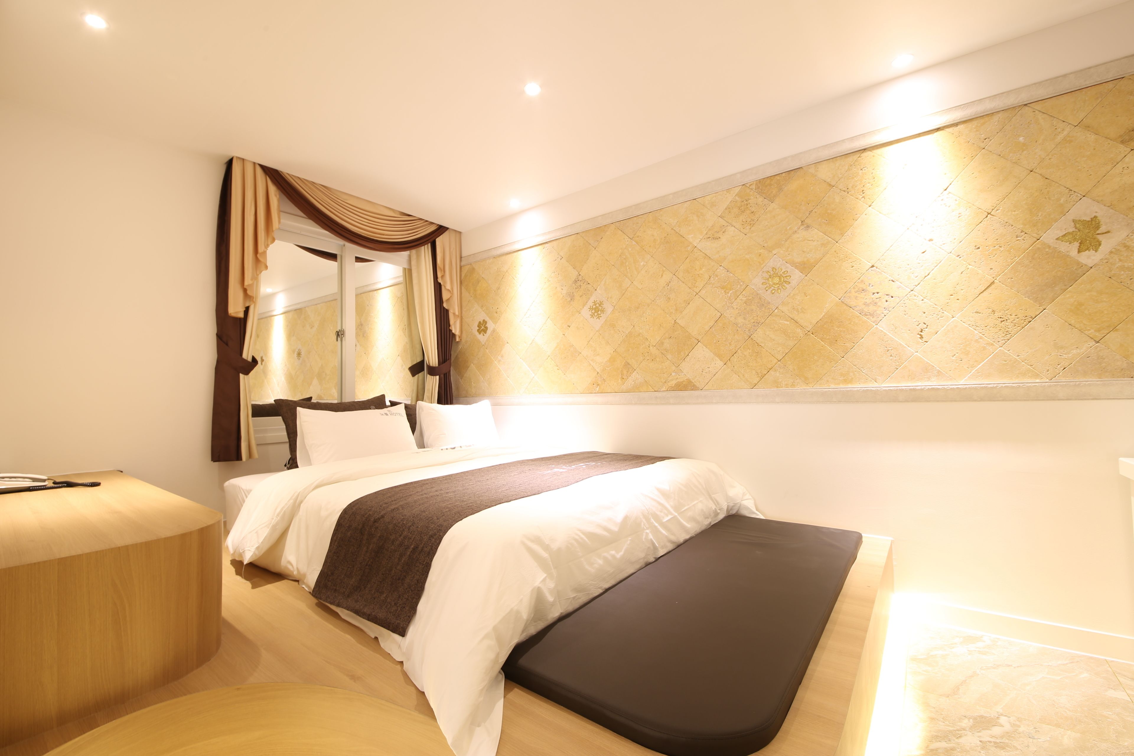 Una habitación de hotel moderna con una cama grande, una mesita de noche y un espejo fijado a la pared.