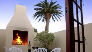 Eine Terrassenausstattung mit Feuerstelle, weißen Plastikstühlen, einem Tisch mit Tischdecke und einem Palmenbaum.