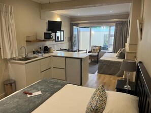 A hotel room with a kitchenette, a bed, a sofa, and a view of the outdoors. - Margate Place Guesthouse (Gqeberha (Port Elizabeth))