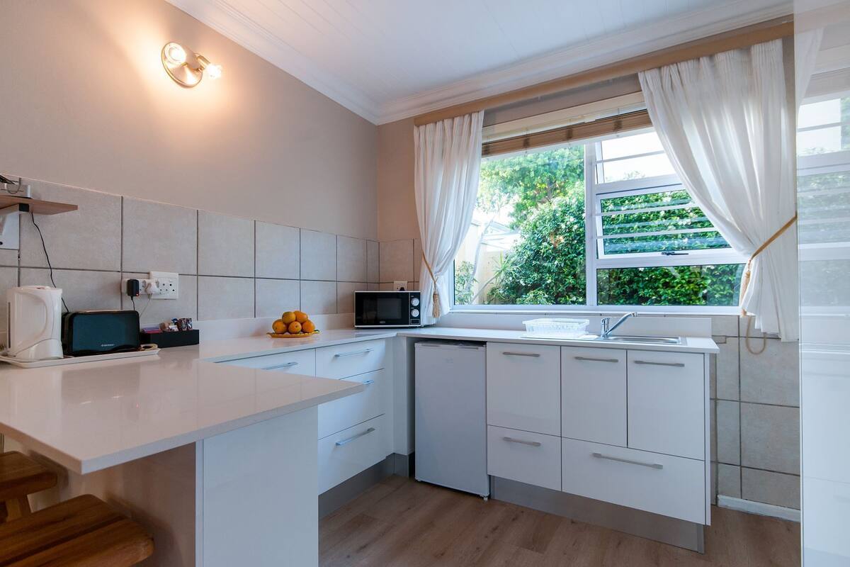 A modern kitchen with white cabinets, a microwave, a sink, and a window with curtains.