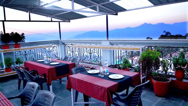 An outdoor terrace with tables and chairs, potted plants, and a view of distant mountains. - Hotel Kishna Palace (Dehradun)