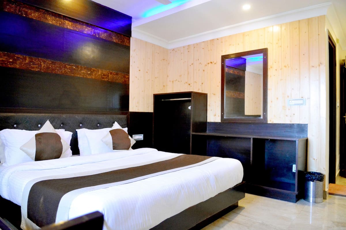Habitación de hotel con una cama grande, cabecera oscura, panel de pared de madera, espejo y un cesto de basura pequeño.