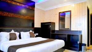 A hotel room with a large bed, a dark headboard, a wooden wall panel, a mirror, and a small trash can. - Hotel Kishna Palace (Dehradun)