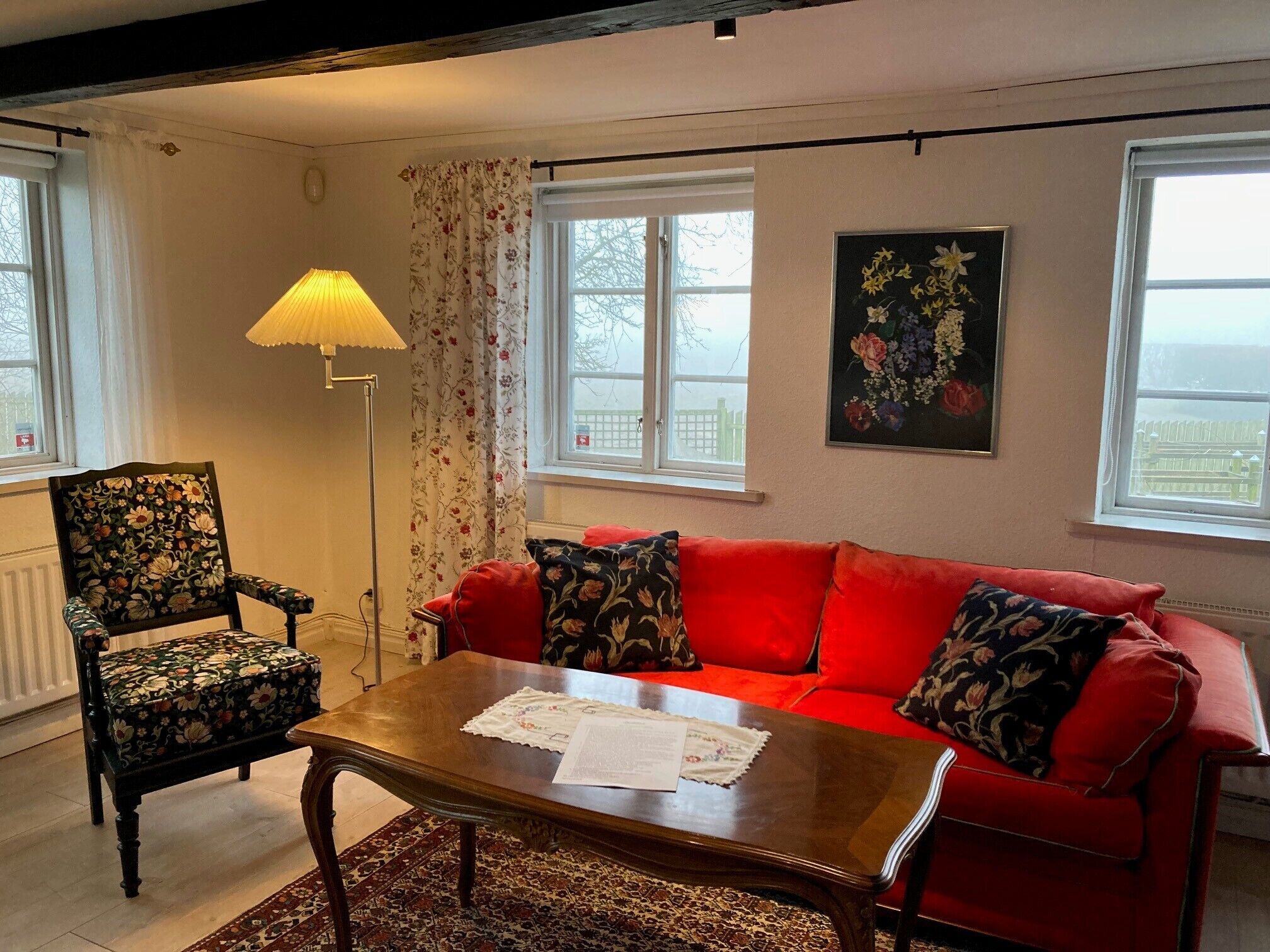 A living room with a red sofa, a wooden coffee table, a floral armchair, and a floor lamp.