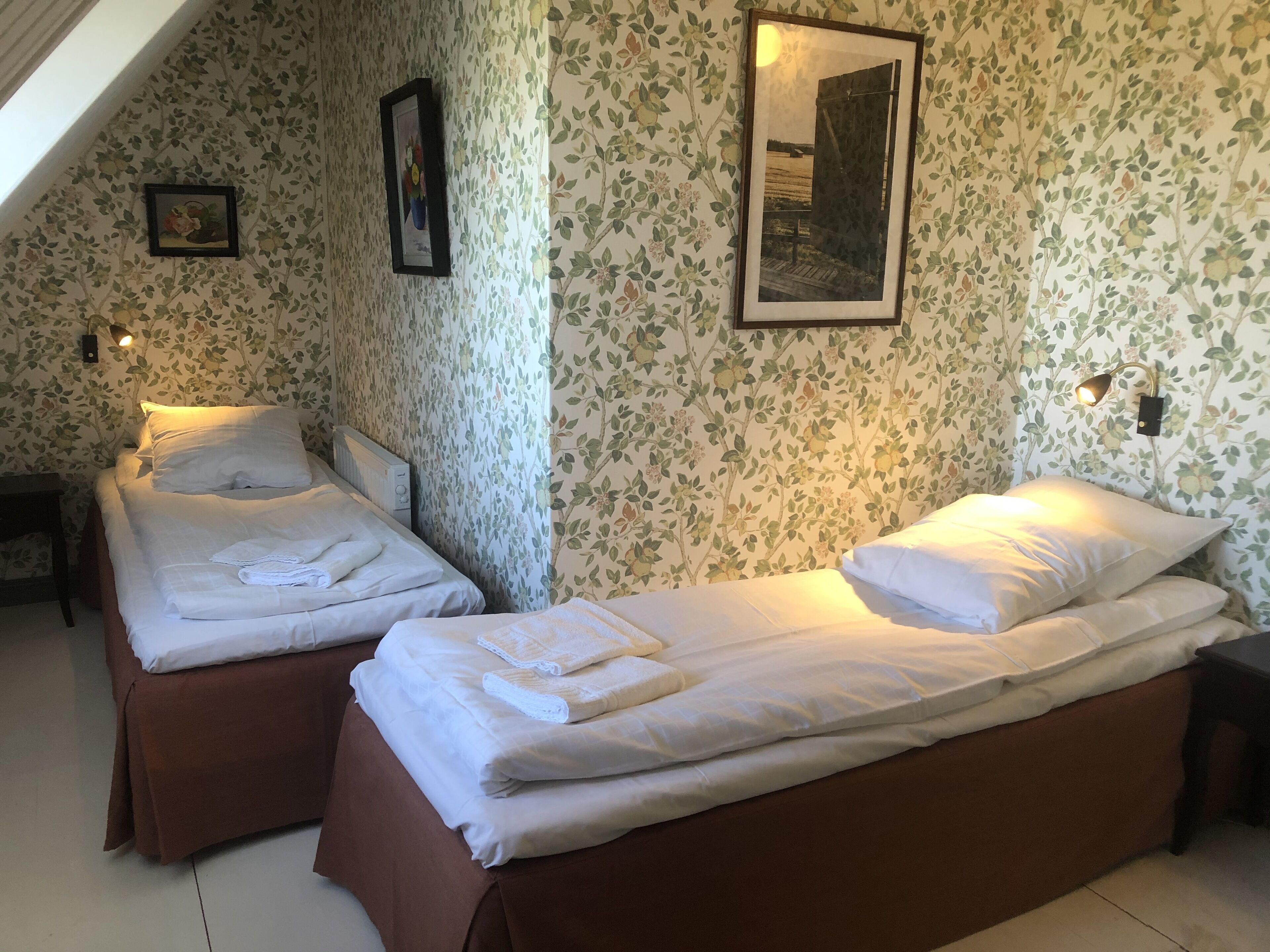 A bedroom with two single beds, a large mirror, and floral wallpaper.