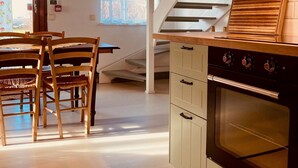 A kitchen with a wooden ceiling, a staircase, and a dining area with wooden chairs and a table.