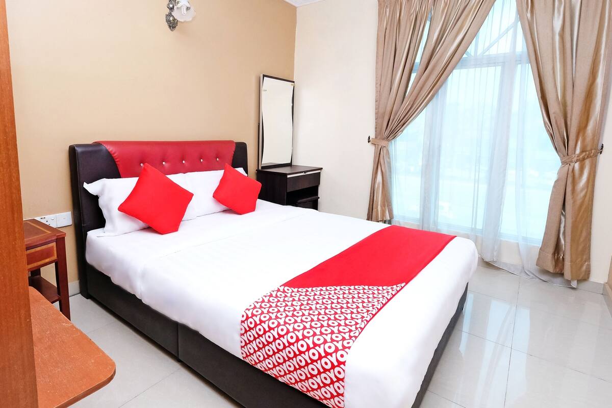 A hotel room with a bed, a nightstand, a mirror, and a window with curtains.