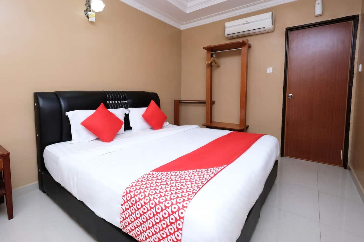 A hotel room with a large bed, a wooden wardrobe, an air conditioning unit, and a door.