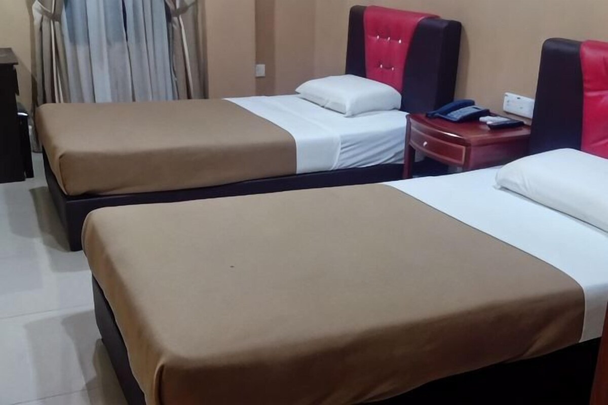 A hotel room with two beds, each with a brown bedspread and white pillows. There is a nightstand with a phone and a book.