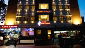 Un hotel de varios pisos con ventanas iluminadas y letreros que dicen 'Hotel Sunshine' y 'Cake Bazaar'.