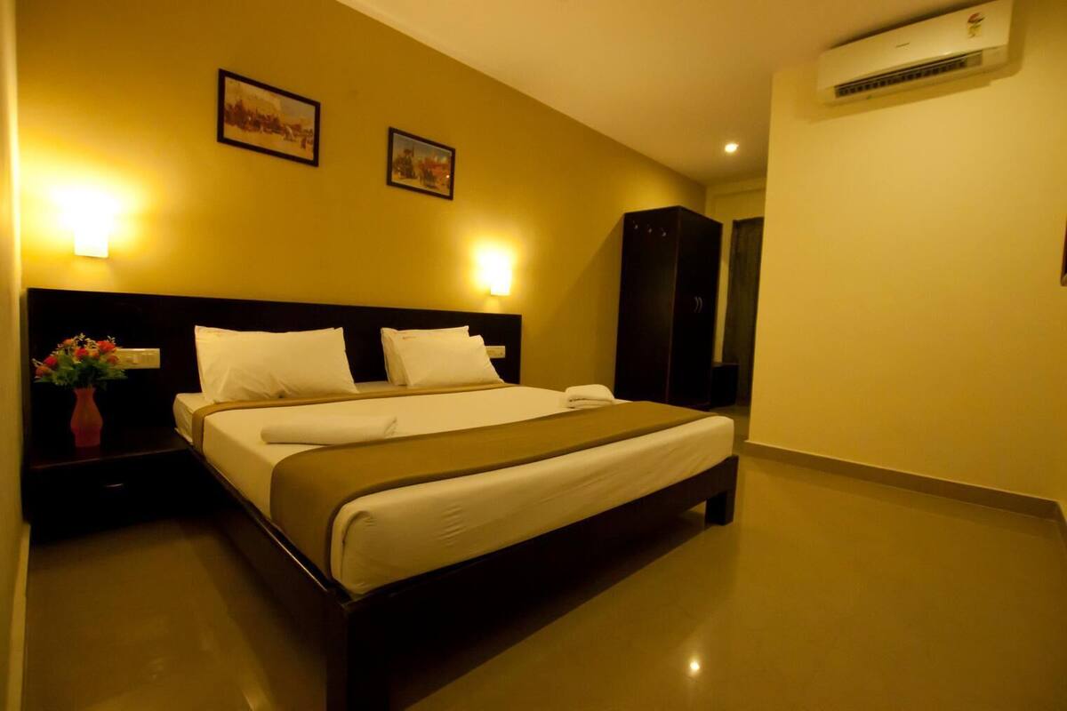 Habitación de hotel con cama, mesitas de noche, un jarrón de flores y dos luces fijadas a la pared.